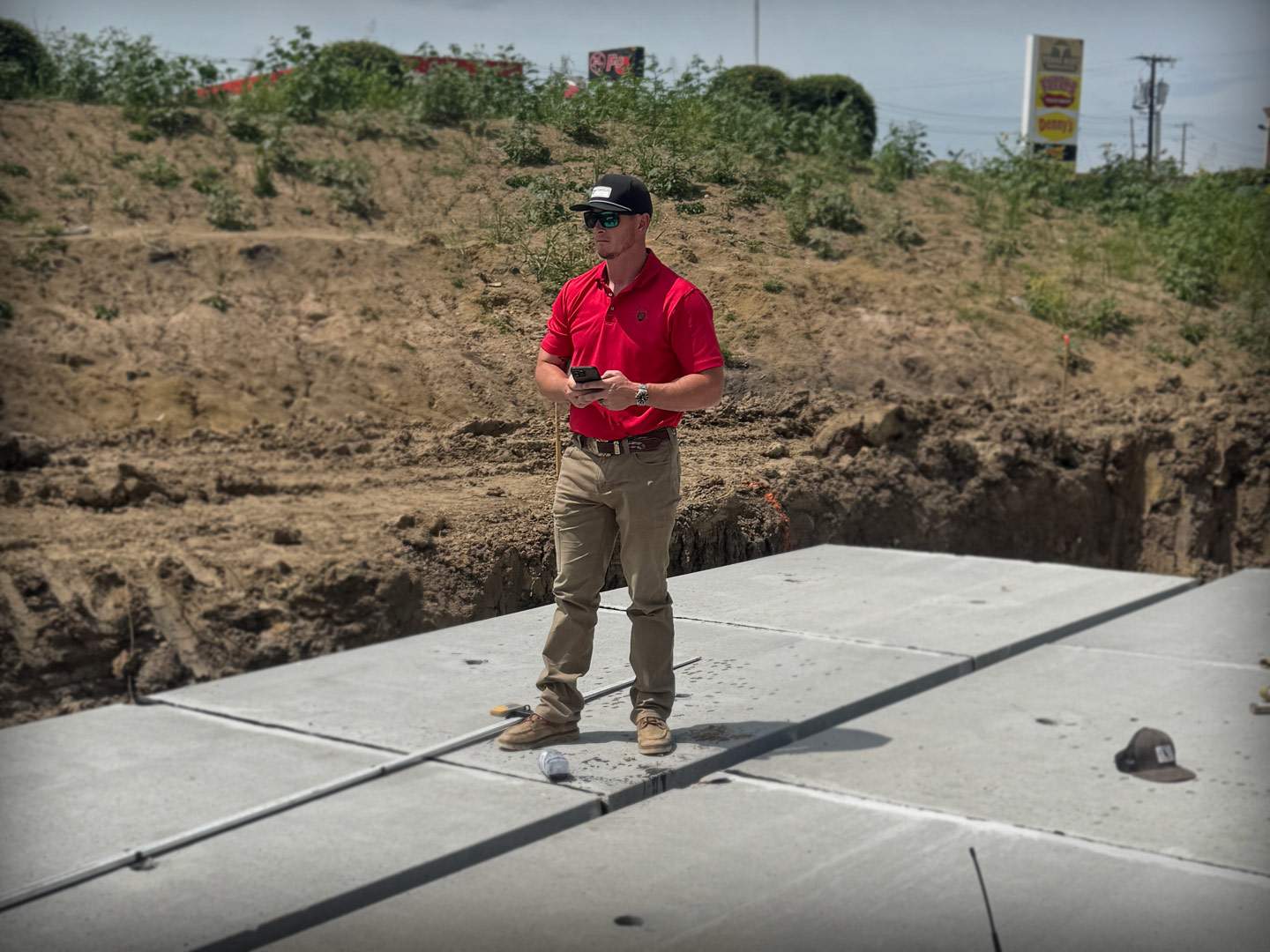 Matt, the Premium Precision operator, on a North Texas site — standing on a poured concrete pad at the edge of a fresh excavation cut.