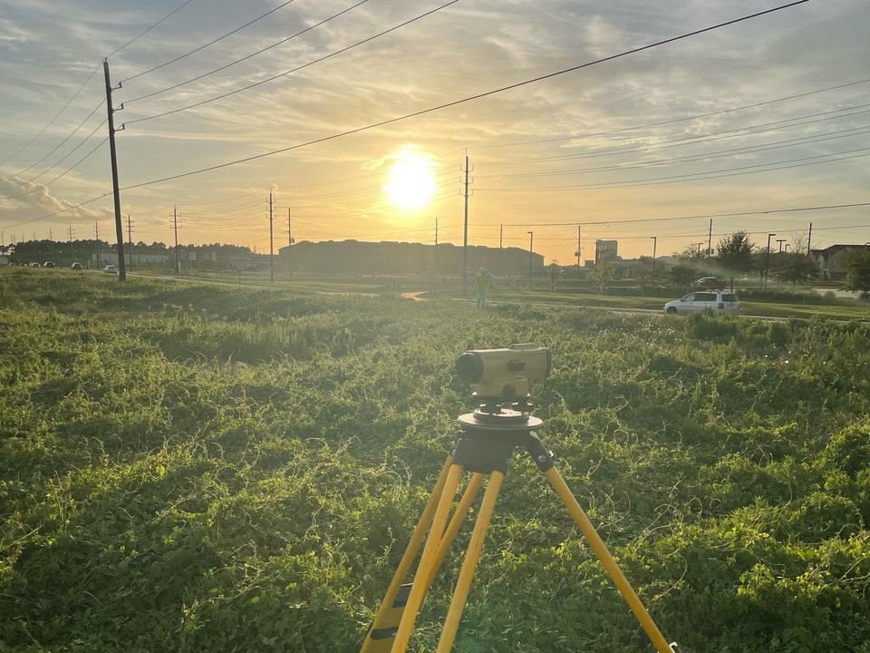 Survey equipment on a tripod in a field at sunset